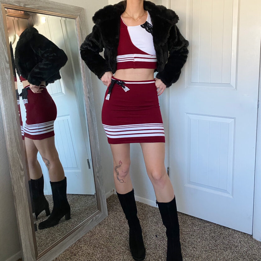 A woman is standing in front of a mirror wearing a red and white cheer skirt.