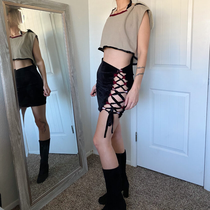 A woman is standing in front of a mirror wearing a crop top and black skirt.