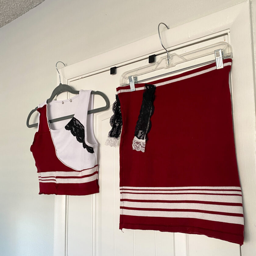 Two red and white cheerleader outfits hanging on a door.