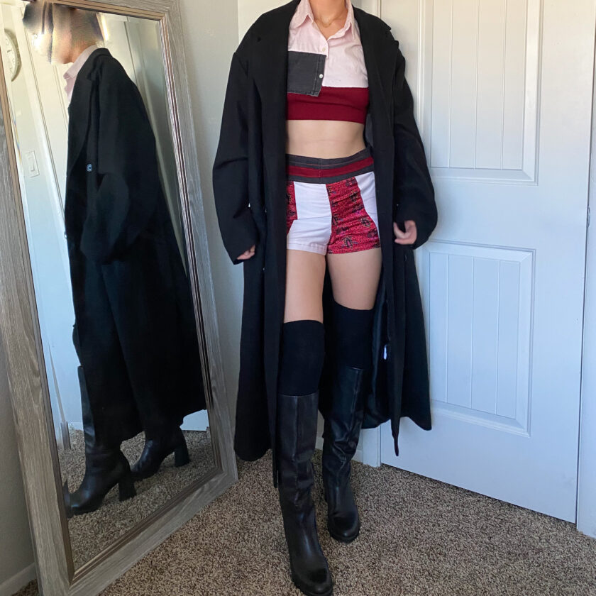 A woman in a black coat and shorts is standing in front of a mirror.