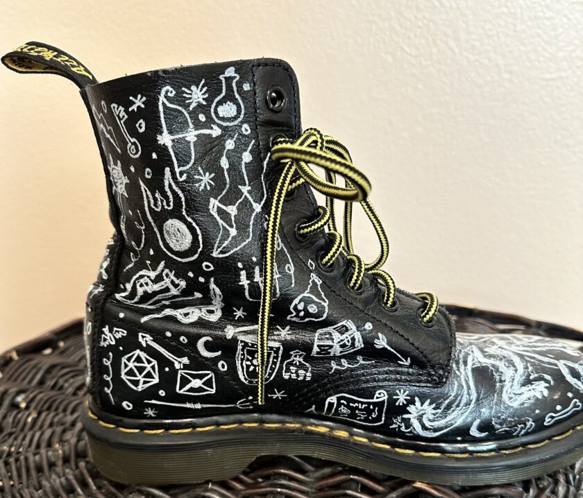 A pair of black dr martens boots with doodles on them.