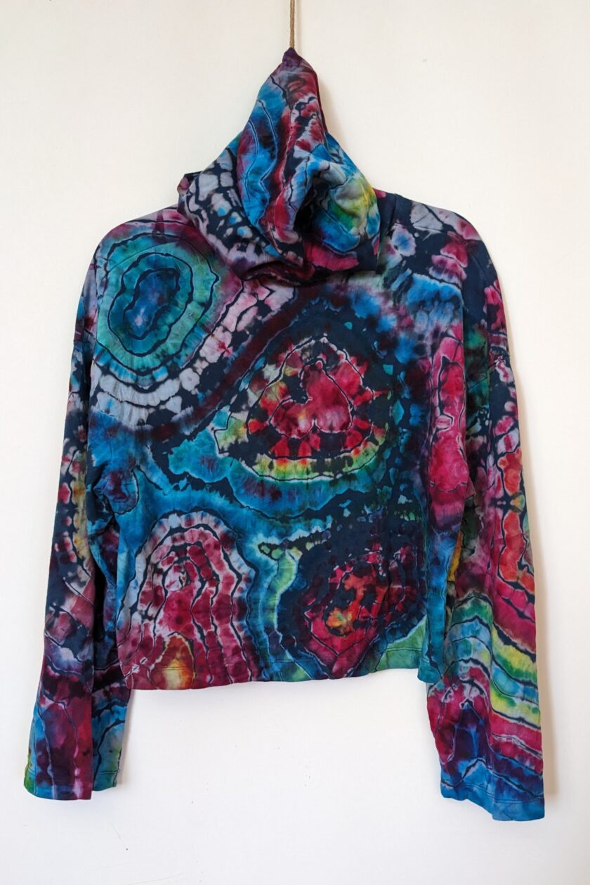 A colorful tie dye hoodie hanging on a wall.