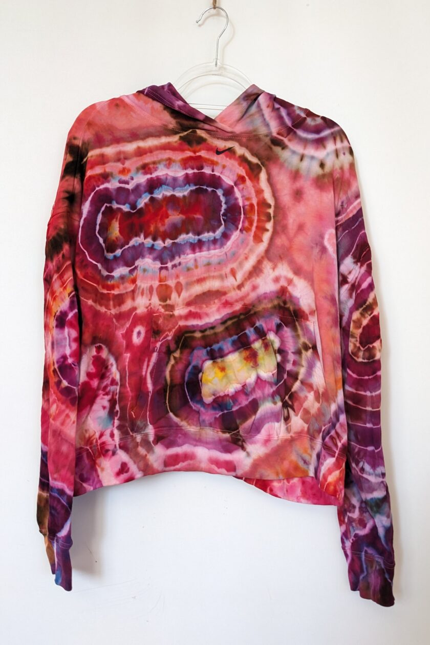 A pink and purple tie dyed sweatshirt hanging on a hanger.
