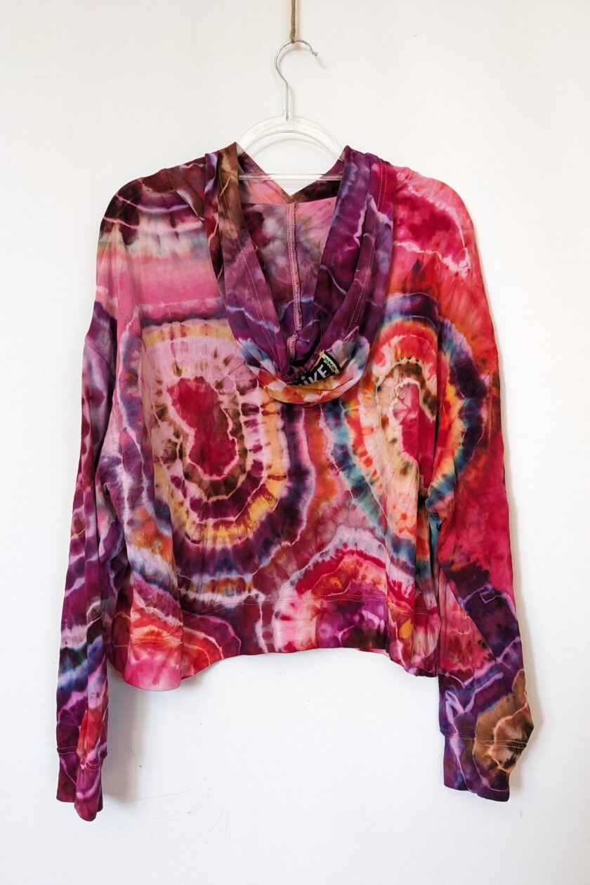 A pink and purple tie dye top hanging on a hanger.