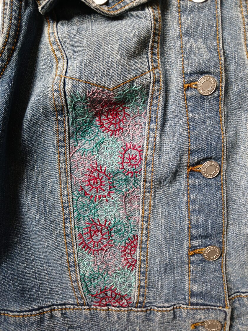 A denim vest with embroidered spirals on it.