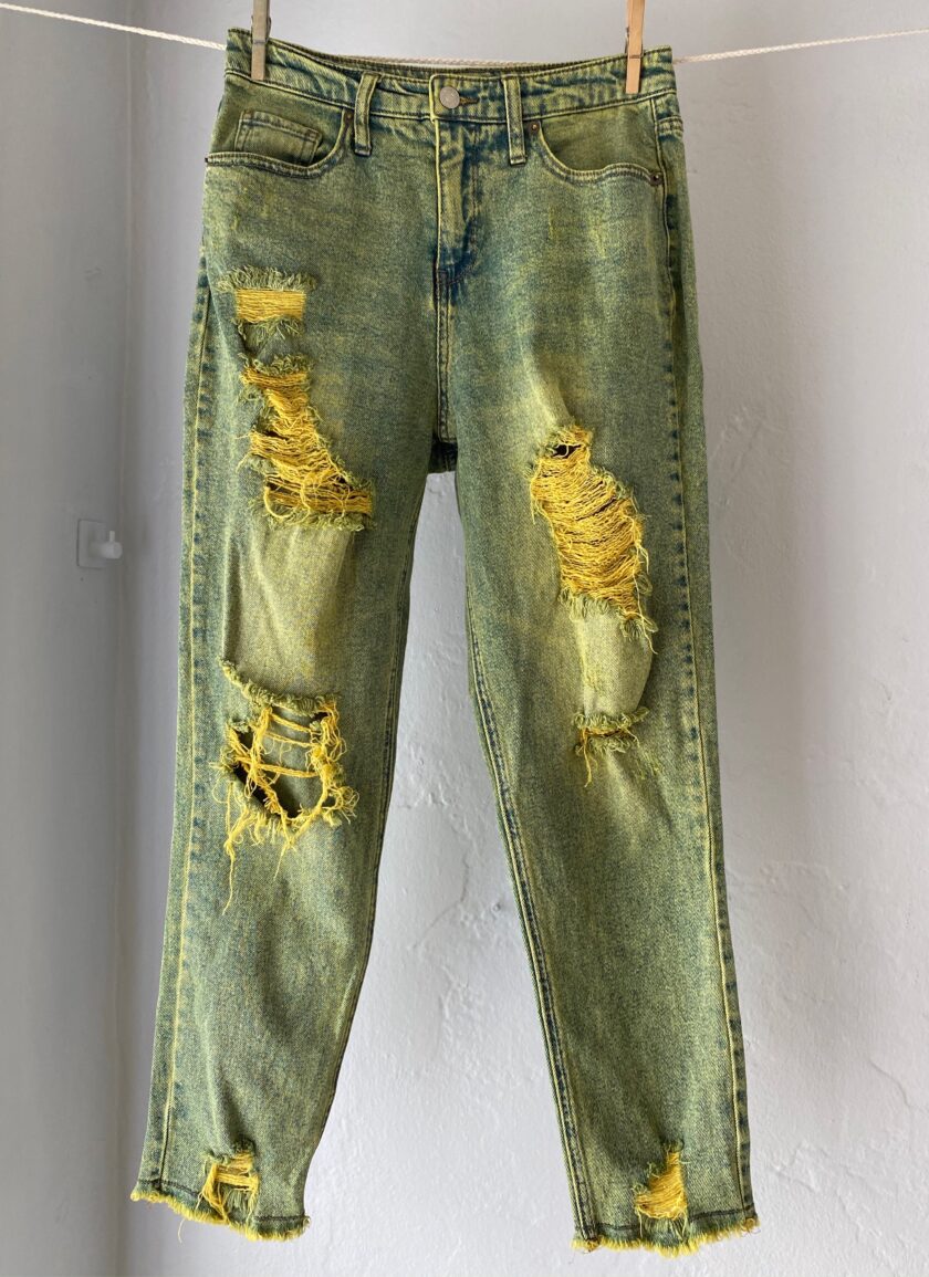 A pair of green ripped jeans hanging on a clothes line.