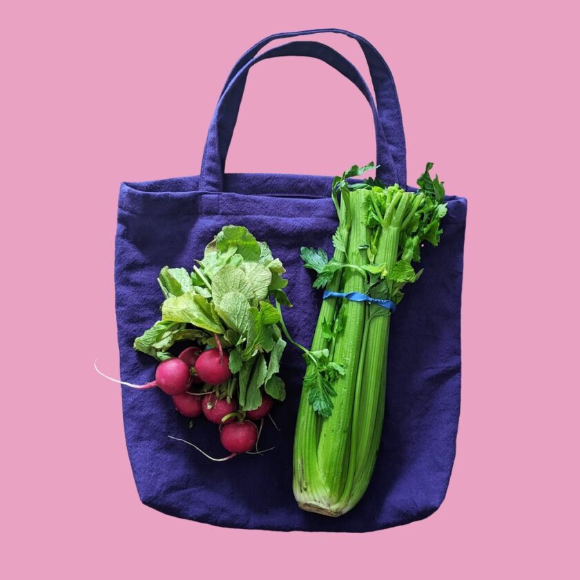 Radishes and celery in a tote bag on a pink background.