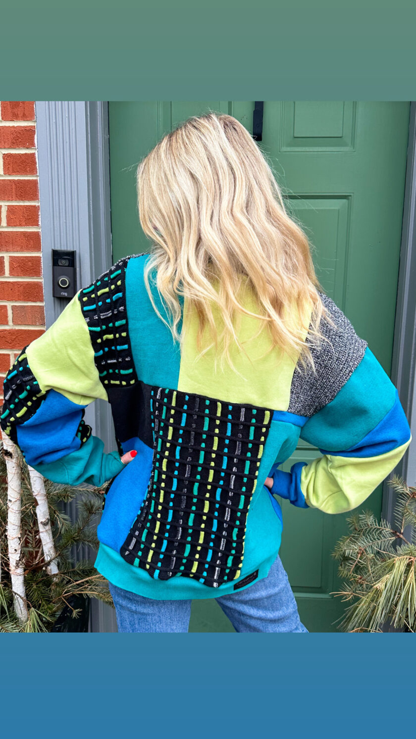 A woman is standing in front of a door wearing a colorful sweater.