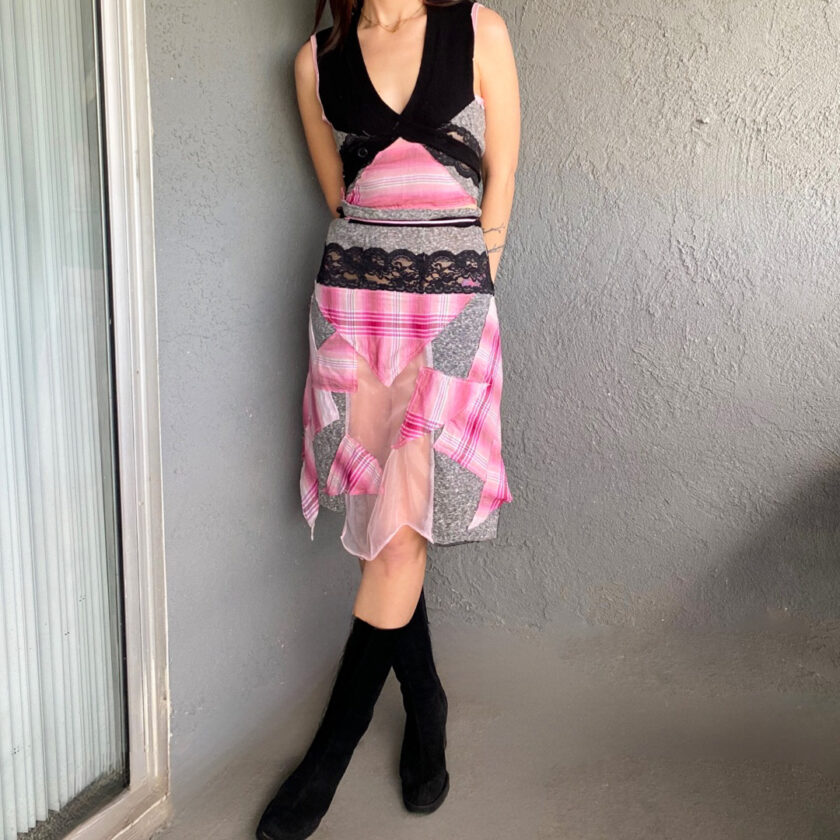 A woman in a pink and black dress is leaning against a wall.