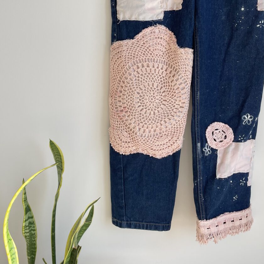 A pair of patched jeans hanging on a plant.