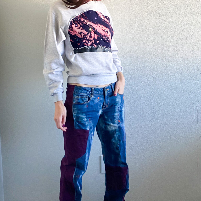 A woman wearing a sweatshirt and jeans standing in front of a wall.