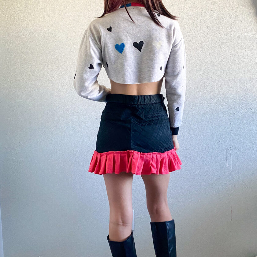 The back of a woman wearing black boots and a cropped sweater with hearts on it.