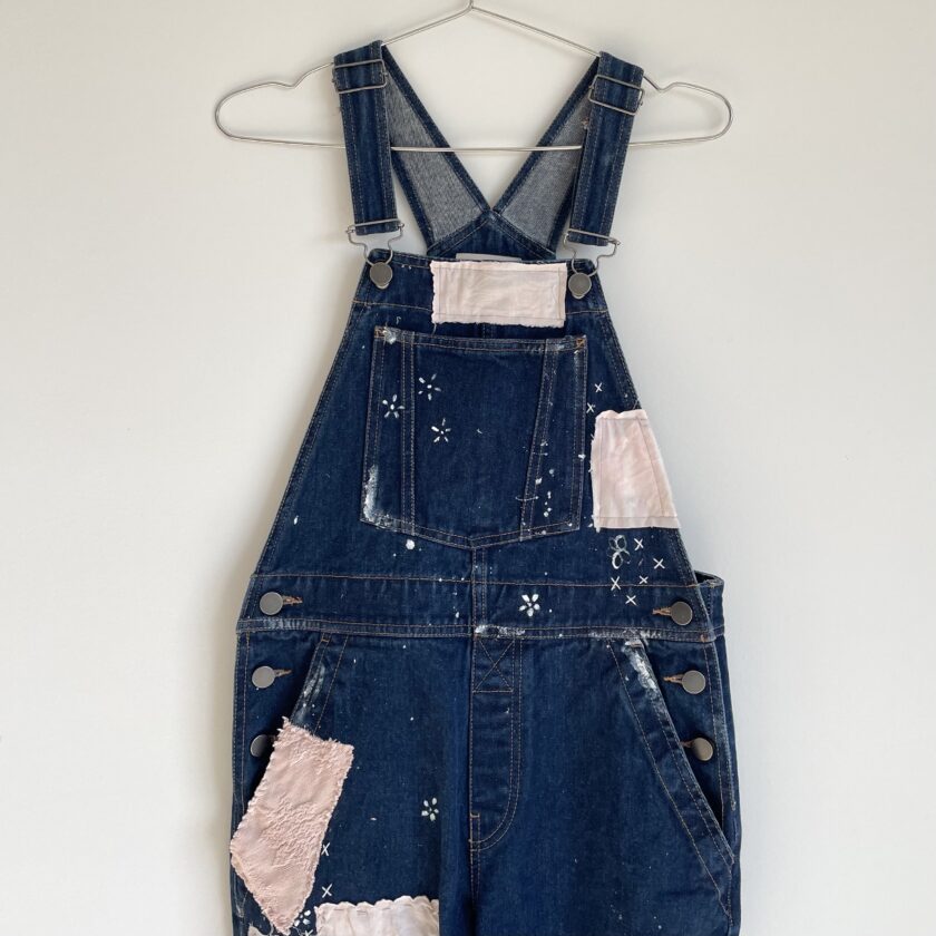 A denim overall with patches hanging on a hanger.