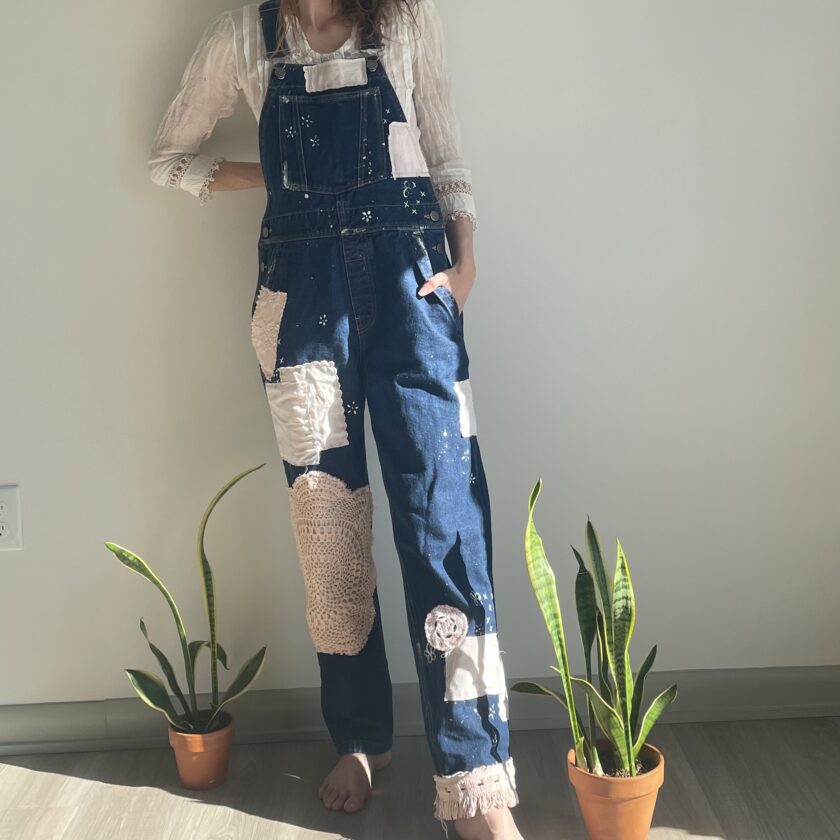 A woman wearing denim overalls standing next to a potted plant.