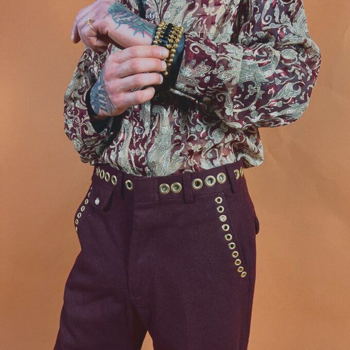 Person in a paisley shirt and burgundy pants with a tattooed hand holding a comb.