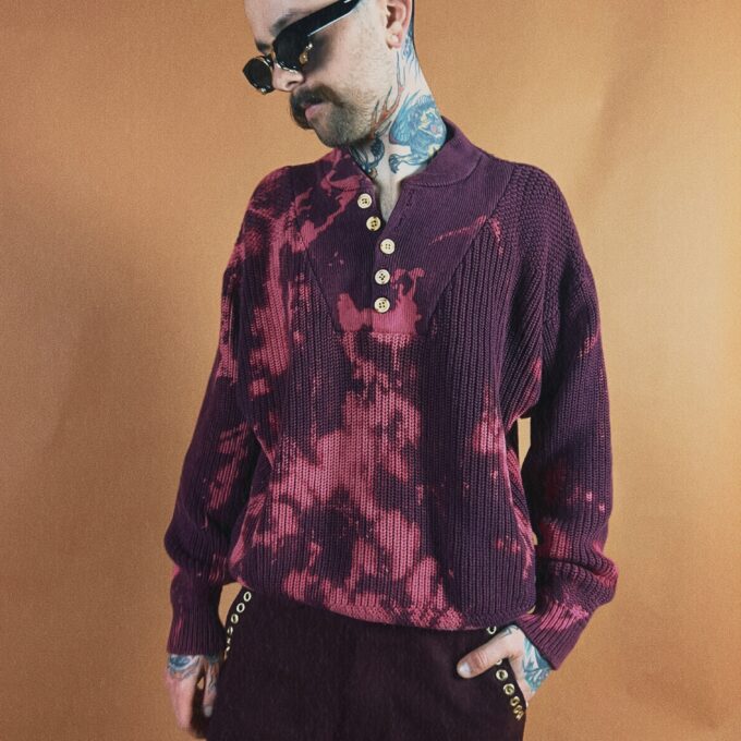 Man with tattoos wearing sunglasses and a patterned sweater.