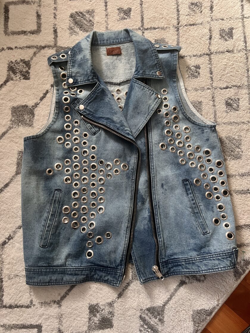 A denim vest with metal grommets laid out on a patterned rug.