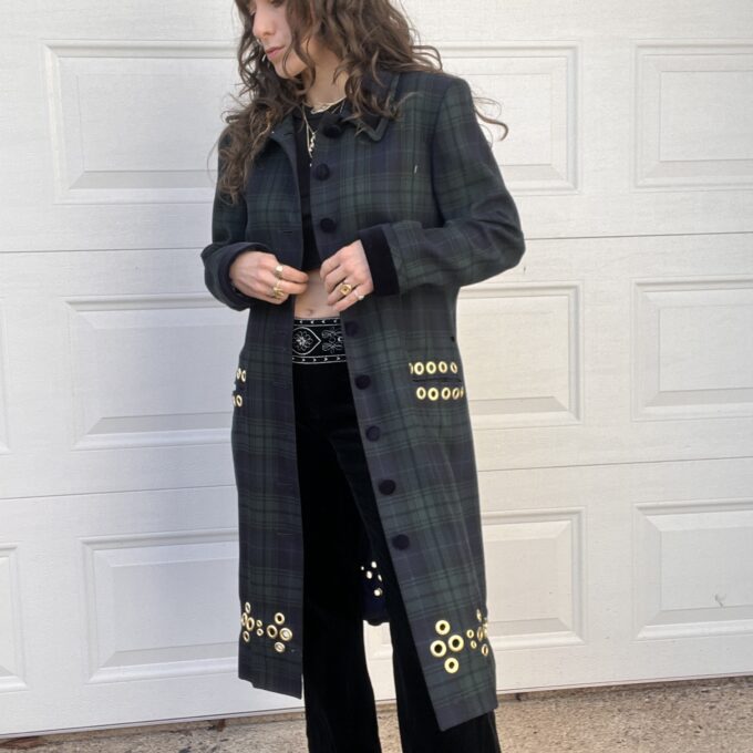 A person in a plaid long coat and black pants standing in front of a white garage door.