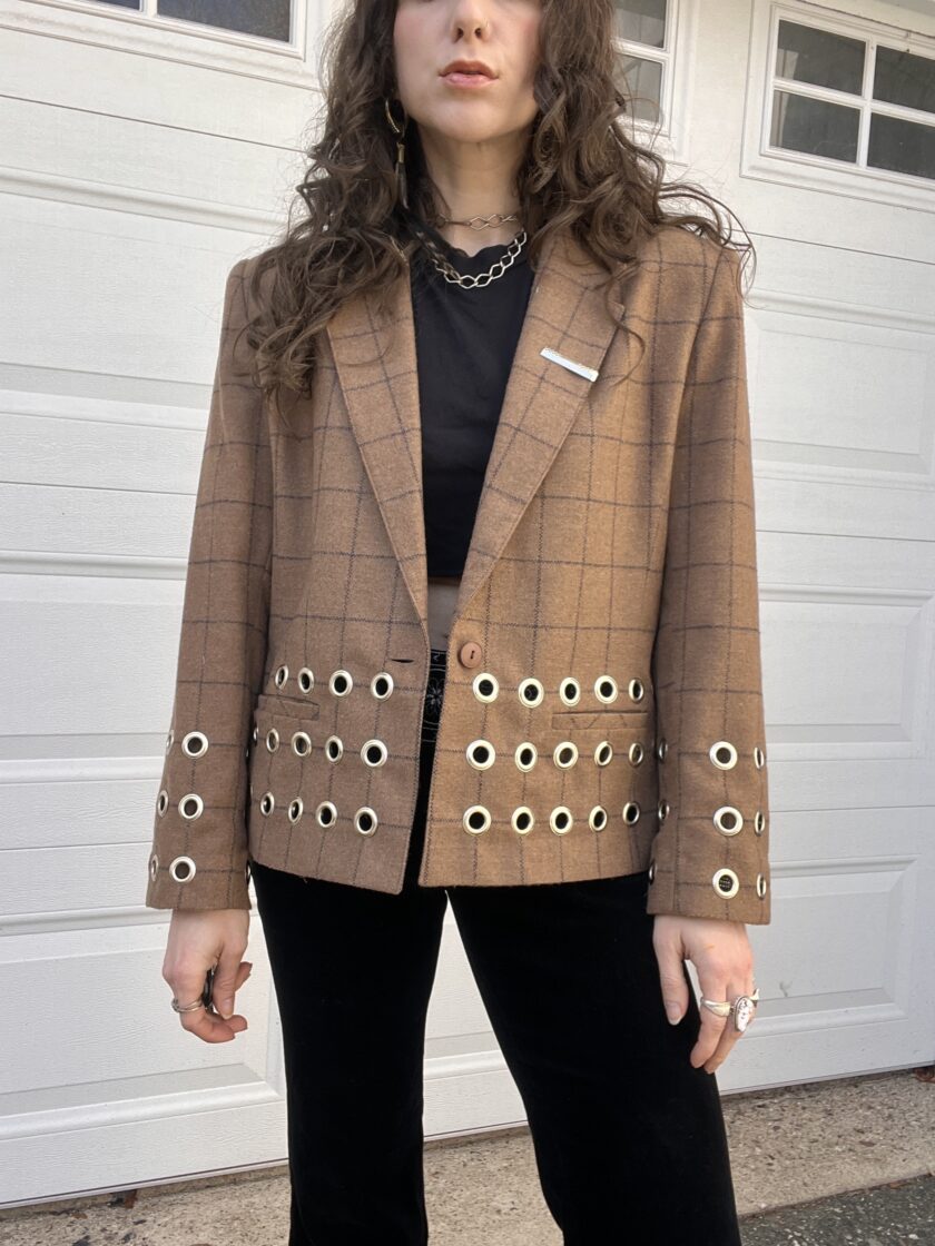 Woman wearing a plaid blazer with grommet details and a black shirt.