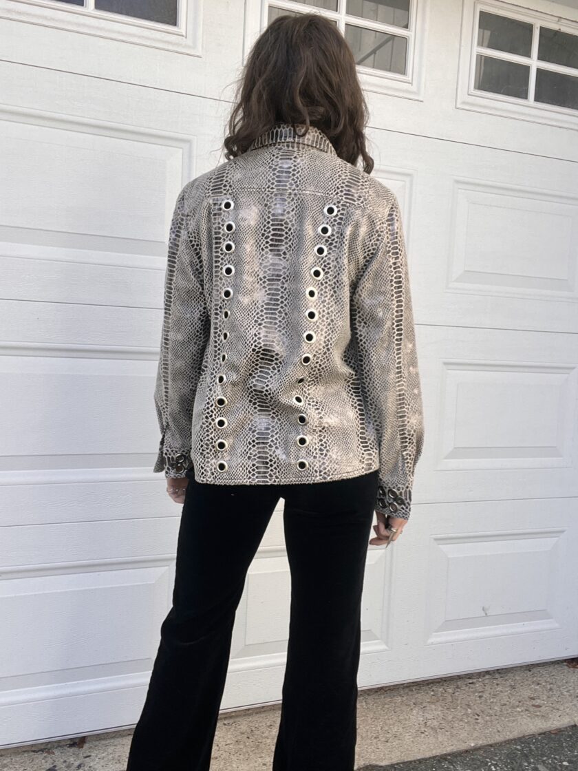 Person standing with their back to the camera wearing a studded jacket and black pants in front of a white garage door.