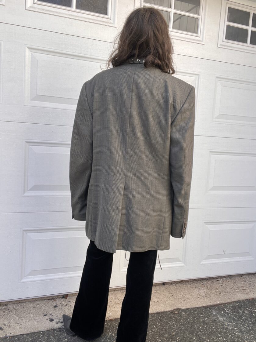 Person standing in front of a white garage door, wearing a grey blazer and black pants.
