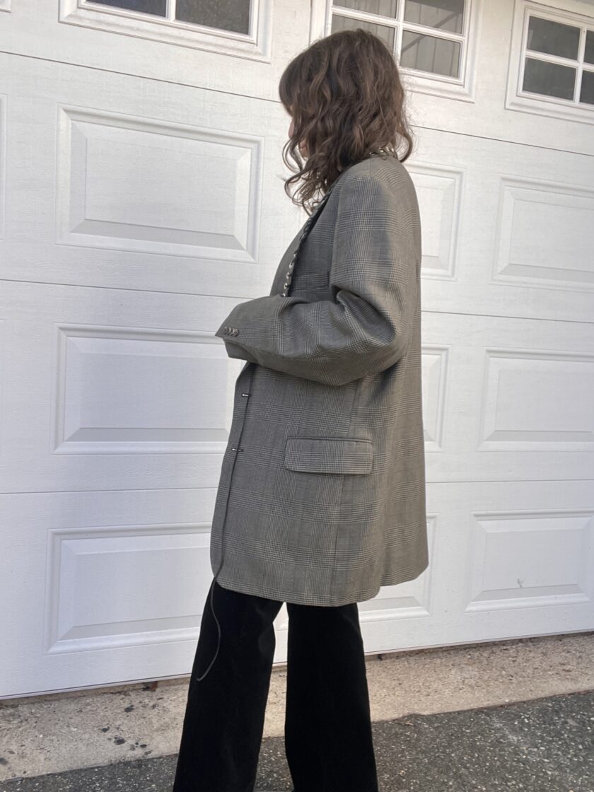 Woman standing in profile wearing a gray blazer and black pants against a white garage door.