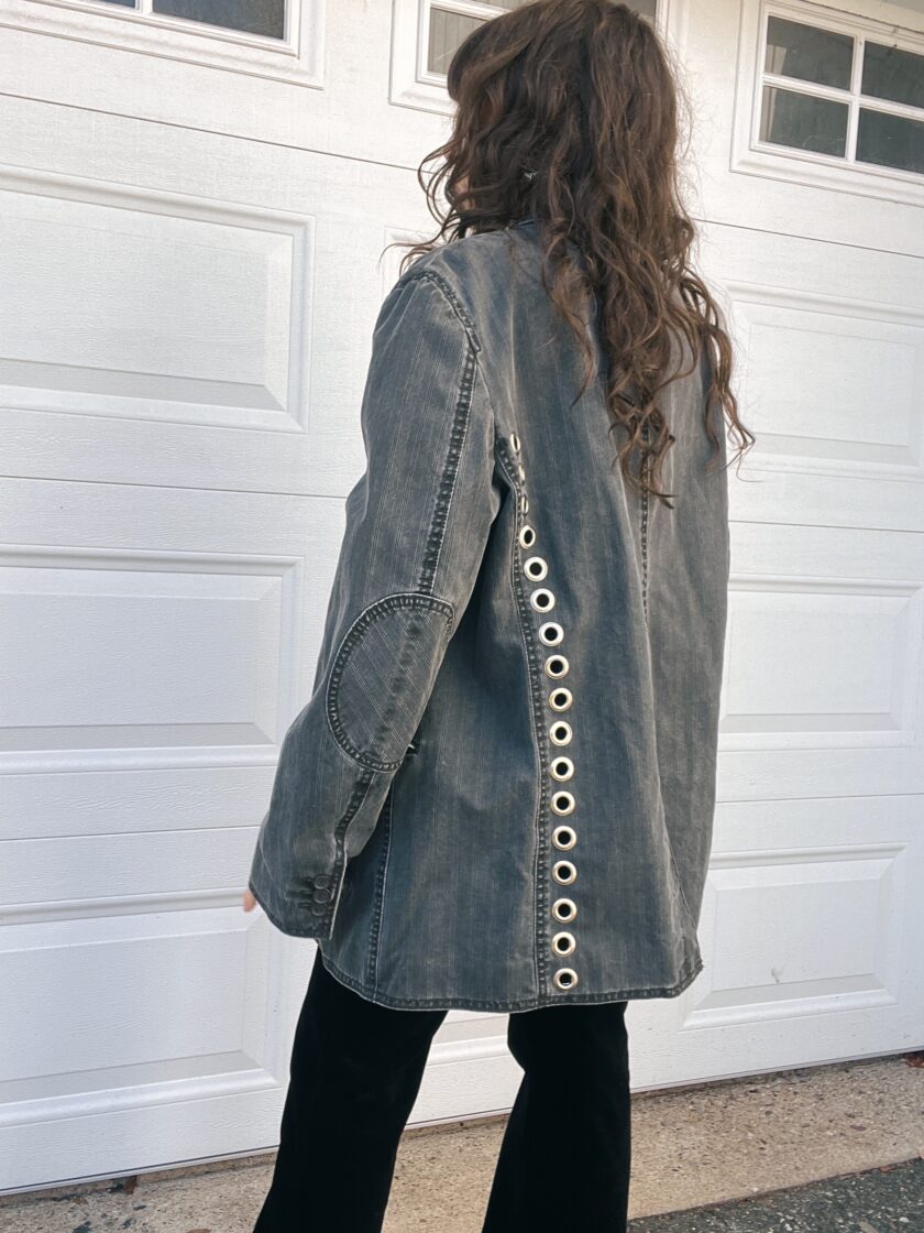 Woman in a denim jacket with grommet details, walking past a garage door.