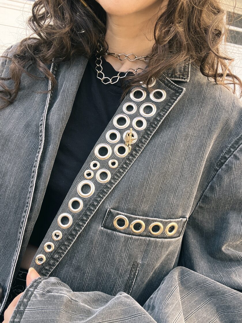 Woman wearing a denim jacket with a unique circular cut-out pattern and grommet details.
