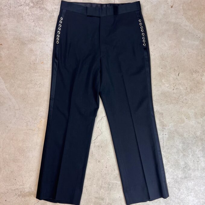 A pair of black trousers with patterned side stripes lying flat on a textured surface.