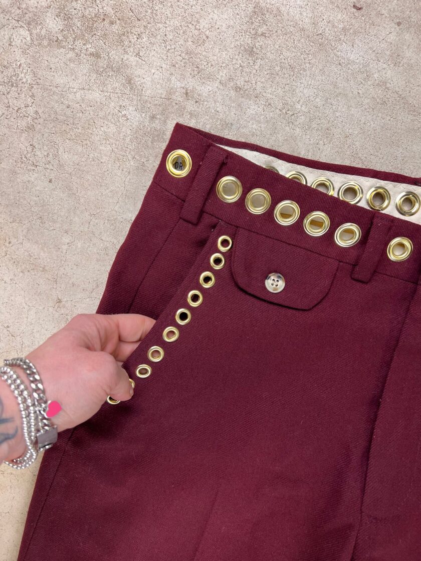 A person holding a burgundy garment with gold grommet detailing.