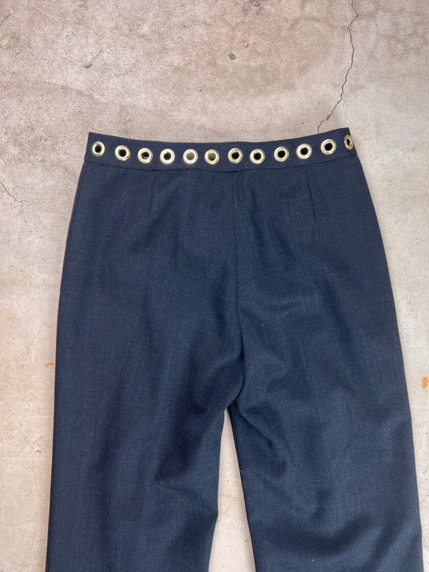Dark trousers with a high waistline featuring a grommet belt detail.