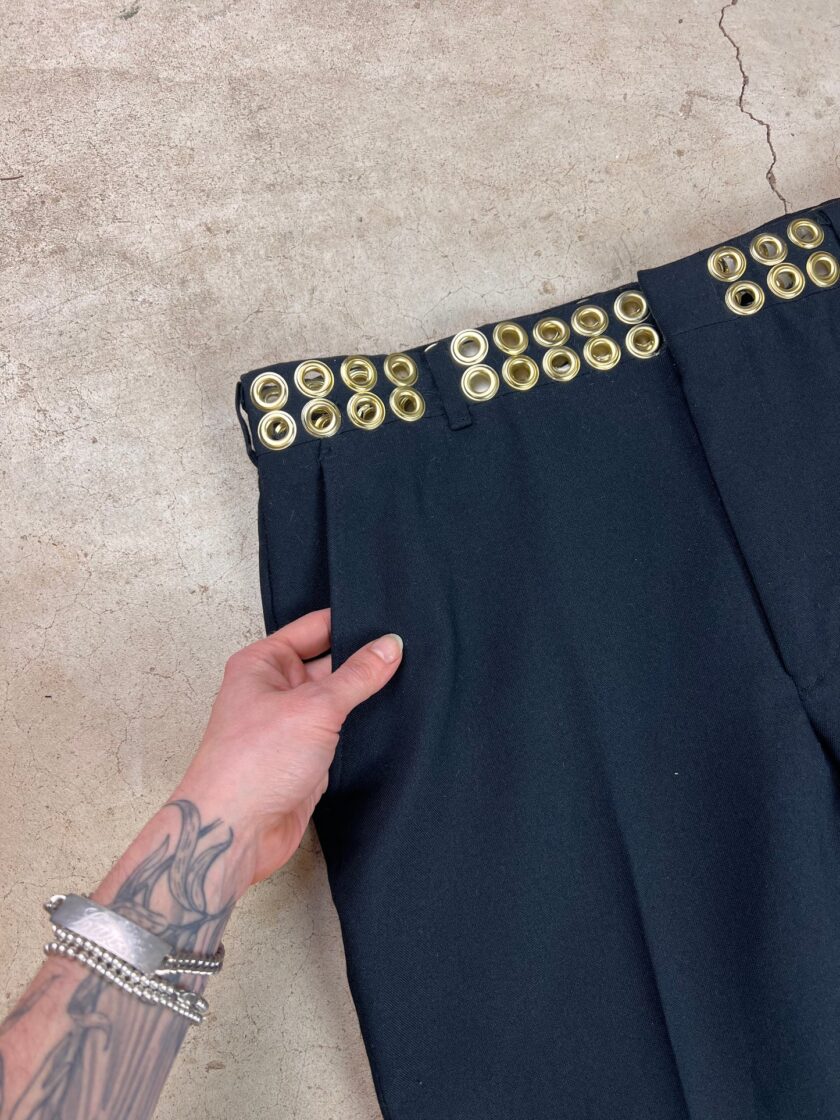 A person holding a black fabric hem adorned with gold eyelets.