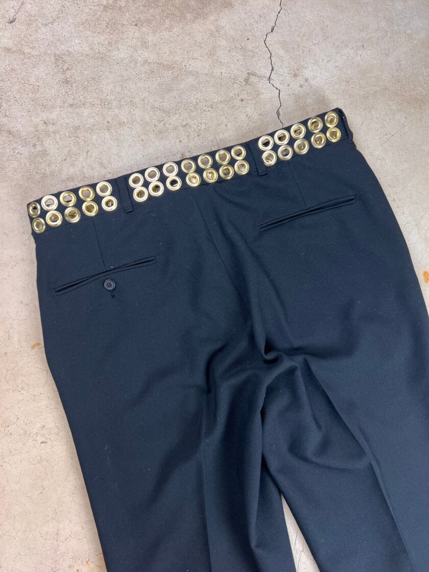 A pair of black trousers with a row of shotgun shells lined along the waistband.
