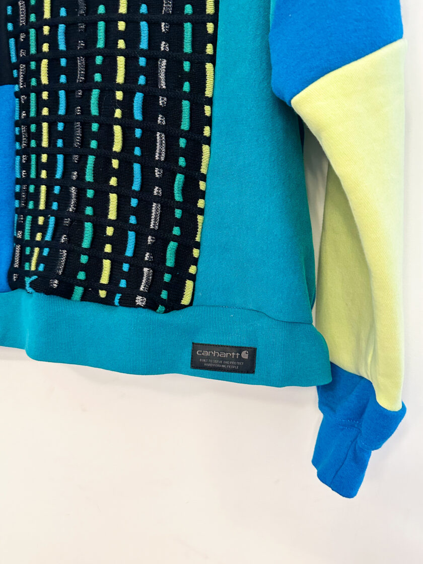 A blue, yellow and green sweatshirt hanging on a wall.