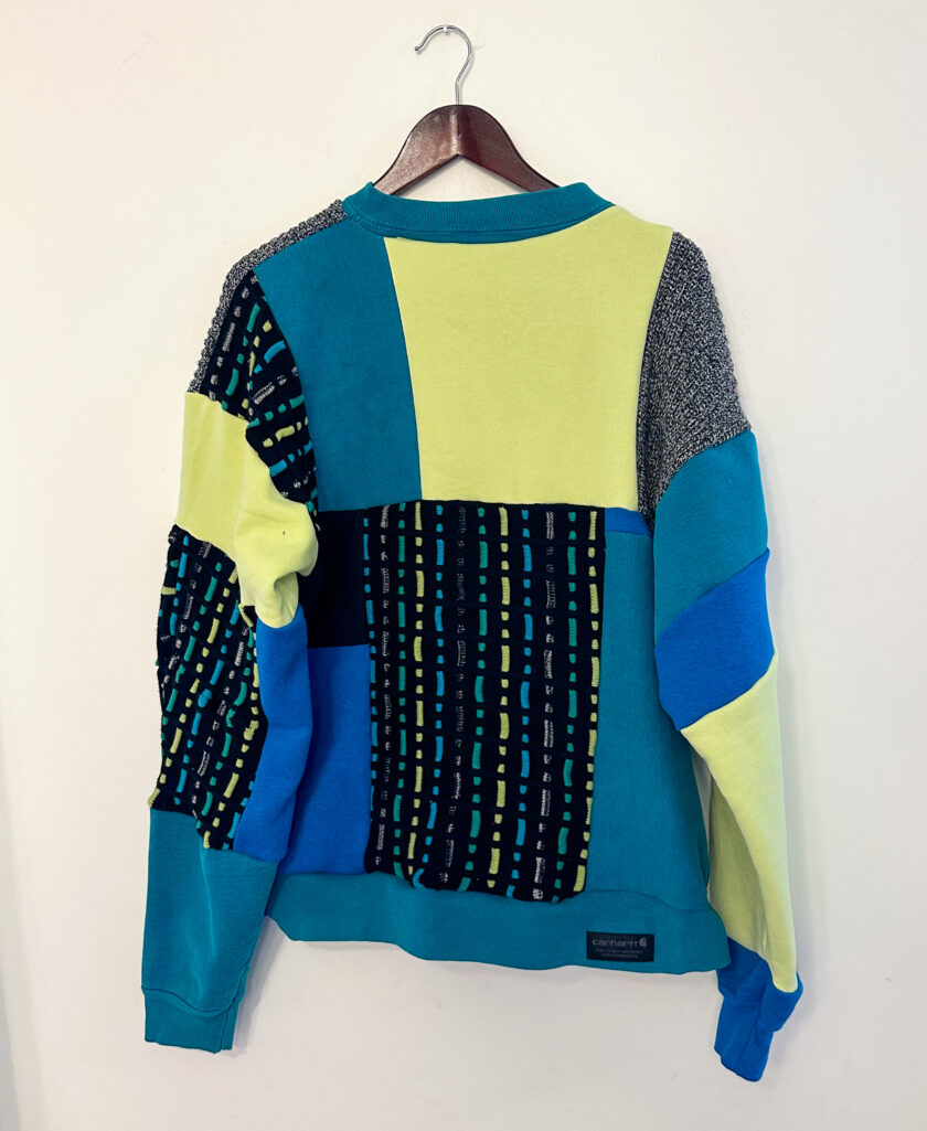A blue, green, and yellow sweater hanging on a wall.