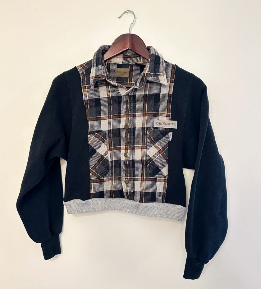 A black and brown plaid sweater hanging on a hanger.