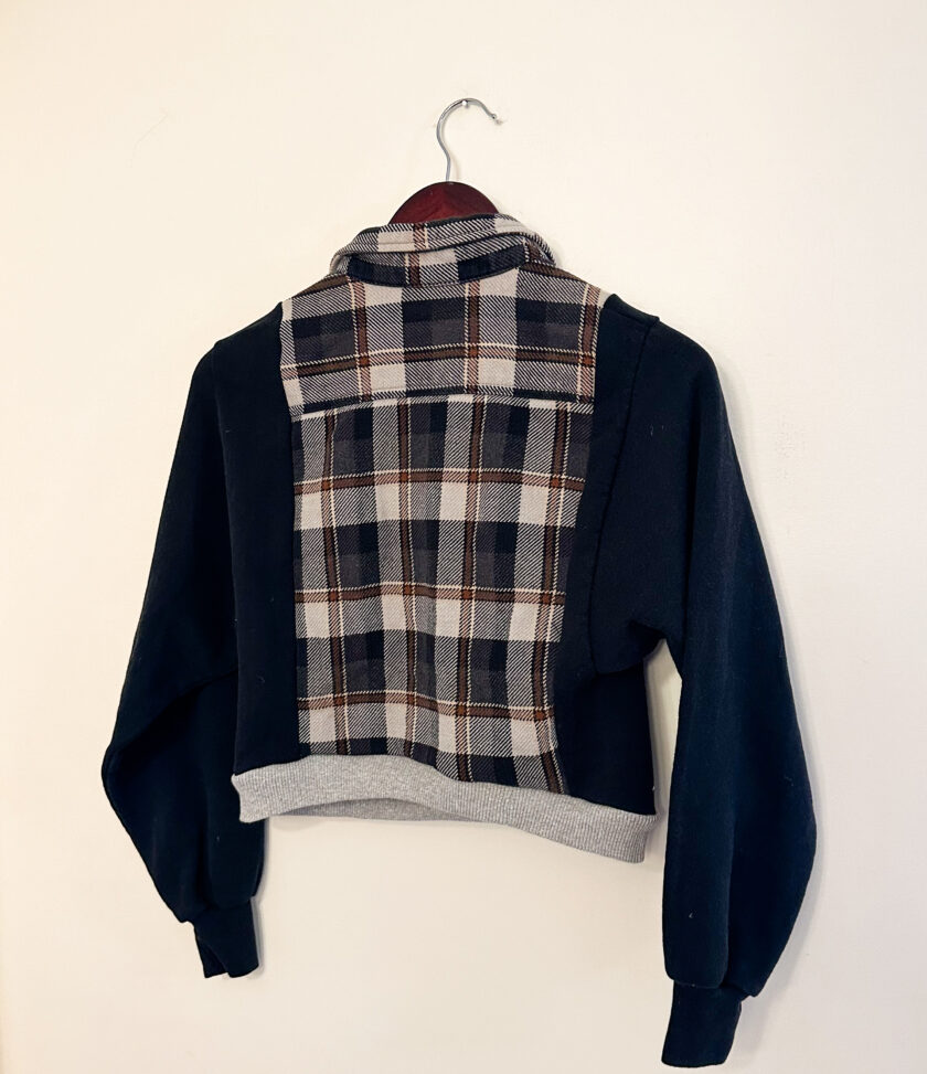 A Carhartt black and gray flannel rework cropped jacket hanging on a wall.