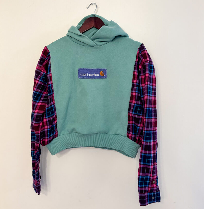 A green and pink plaid hoodie hanging on a hanger.