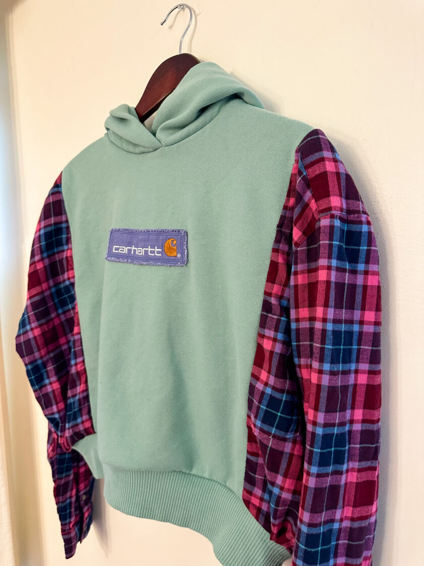 A green and pink plaid hoodie hanging on a wall.