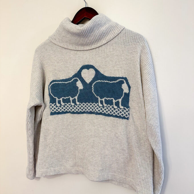 A sweater with sheep on it hanging on a hanger.