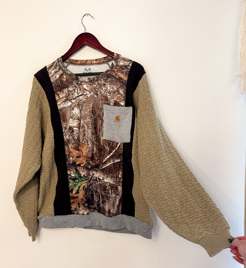 A sweater with a camouflage pocket hanging on a wall.