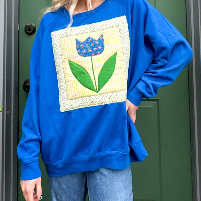 A woman wearing a blue sweatshirt with a flower on it.