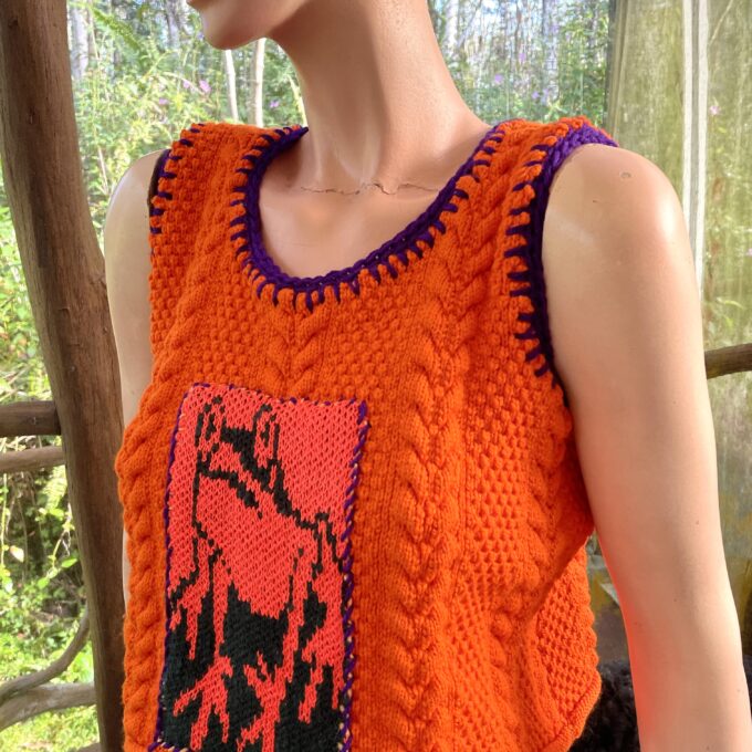 Orange knitted vest with a contrasting black and red patterned design on a mannequin.