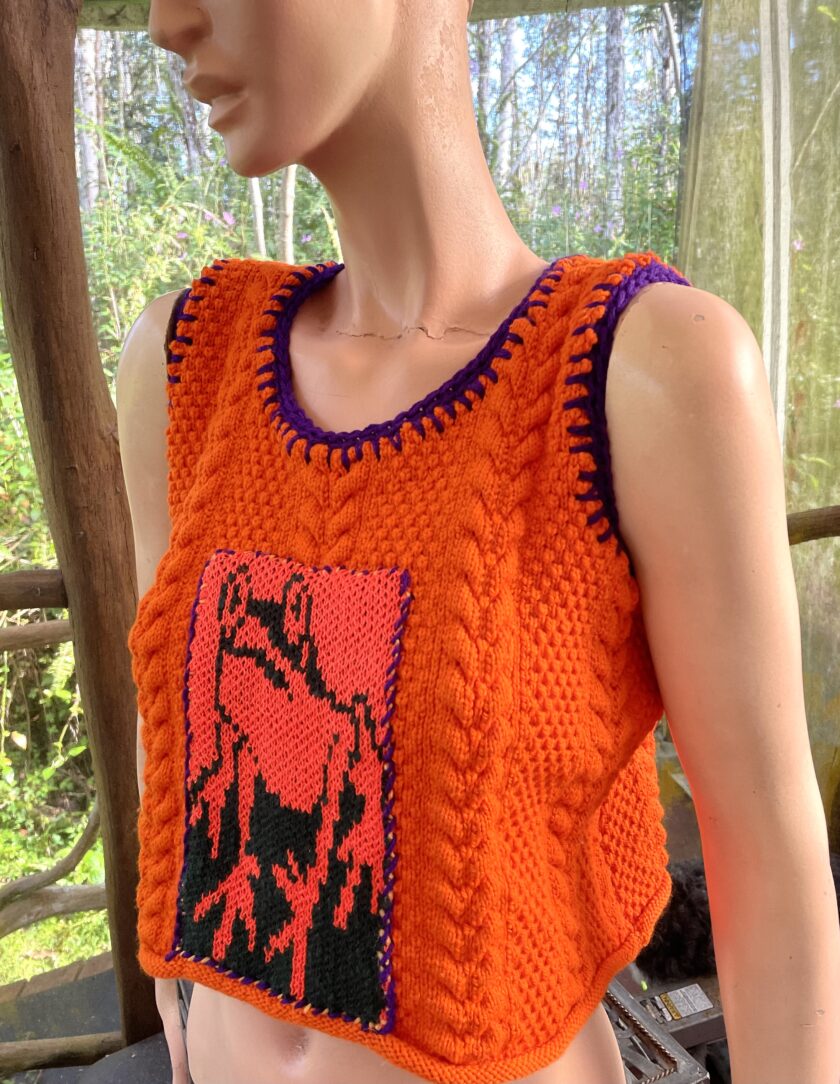 Orange knitted vest with a contrasting black and red patterned design on a mannequin.
