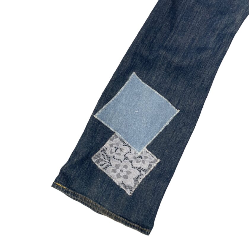 Blue jeans with a patchwork design consisting of a lighter blue patch and lace fabric on a white background.