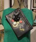 Black shoulder bag with floral design displayed on a green mannequin torso.