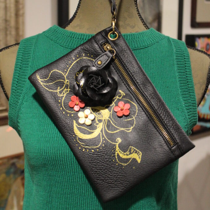 Black shoulder bag with floral design displayed on a green mannequin torso.