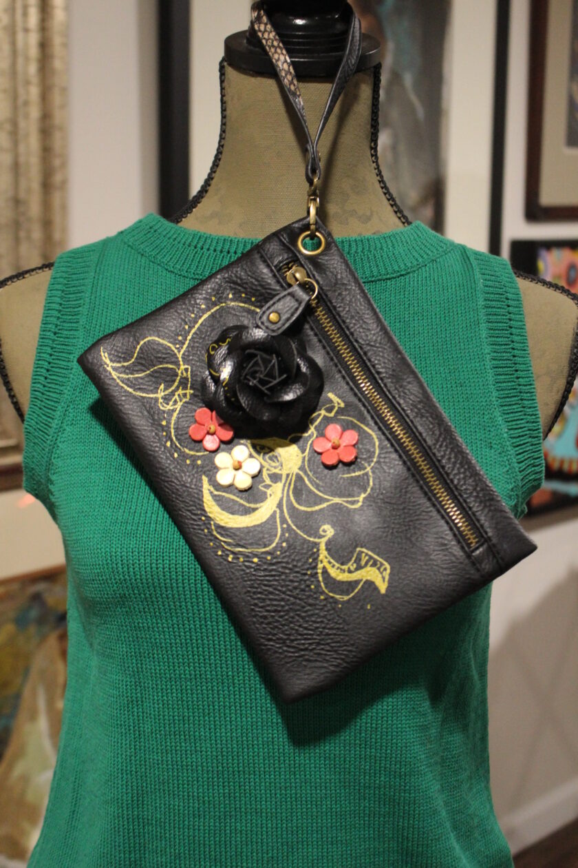 Black shoulder bag with floral design displayed on a green mannequin torso.