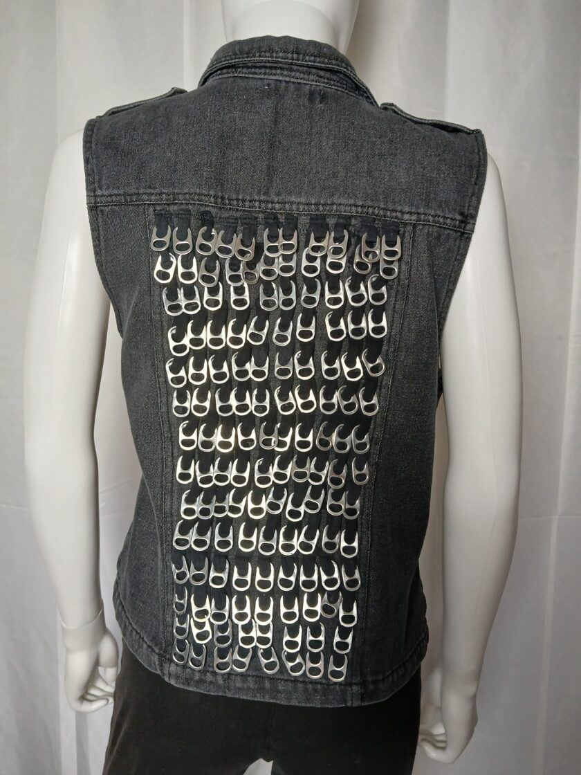 A denim vest with pull tabs arranged in a grid pattern on the back, displayed on a mannequin.