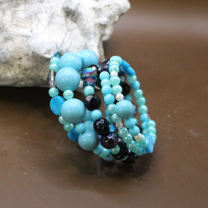 A turquoise and black beaded bracelet displayed on a brown surface next to a white rock.